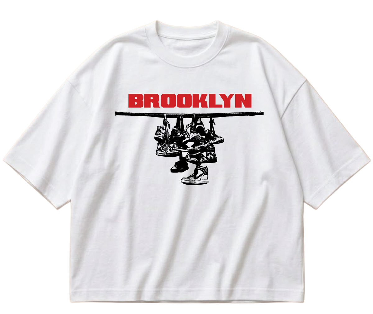 White boxy cropped Sneaker Hang tee with red Brooklyn lettering above a black hanging-sneakers design.